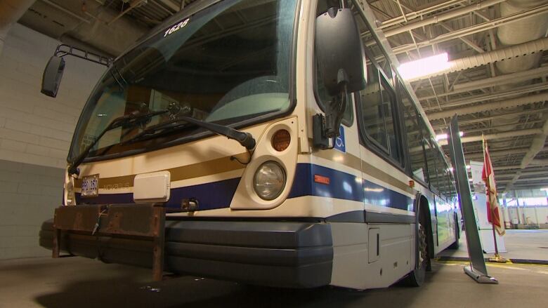 A bus parked inside a large garage. To the right of the bus is a Canadian flag. 