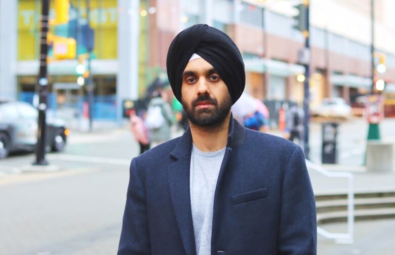 A man wearing a turban stands outside in a city square.