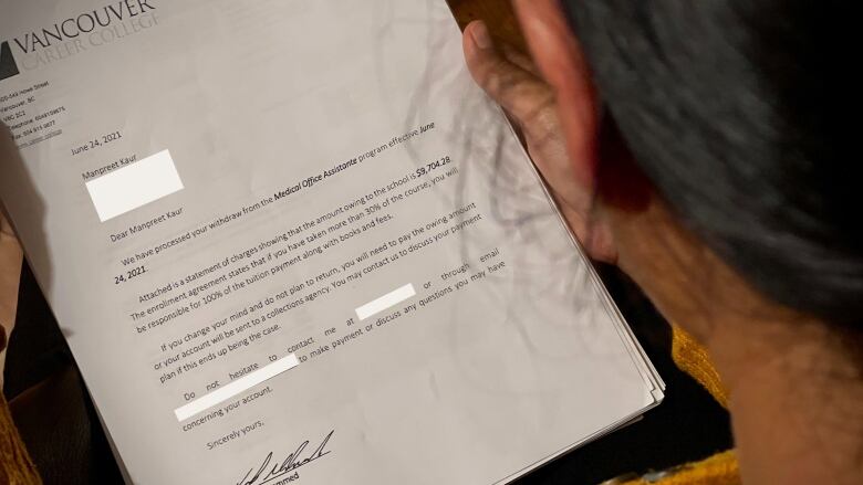 A woman, whose face is obscured, reads a letter from Vancouver Career College.