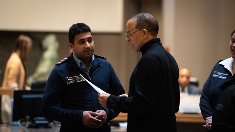 A man reads from a sheet of paper while a security guard looks on.