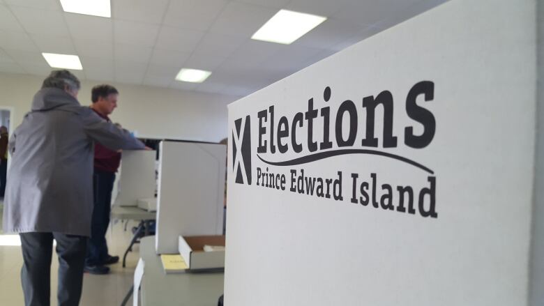 Prince Edward Island Elections sign at polling station, people placing ballots in the background.