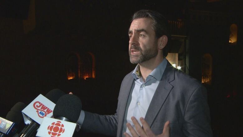 Man speaks with reporters in dark lit room