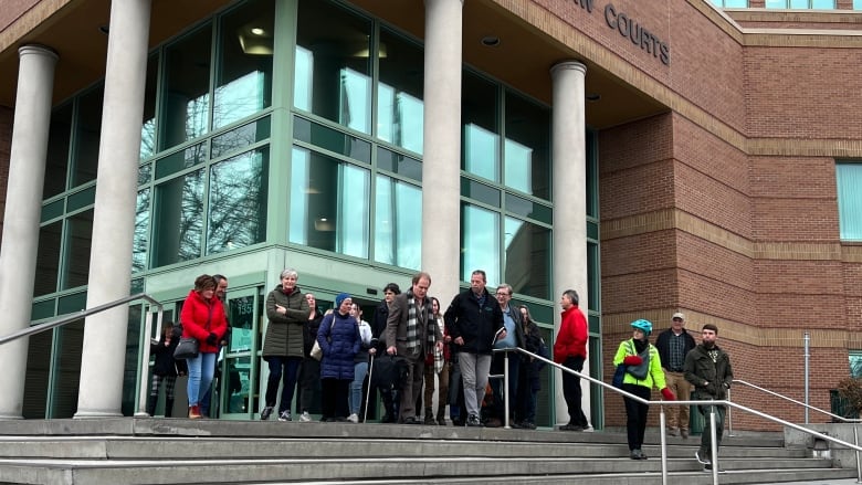 A man carrying wearing a suit jacket and pants and carrying a briefcase is seen leaving the Kelowna courthouse with about 20-30 supporters following him.