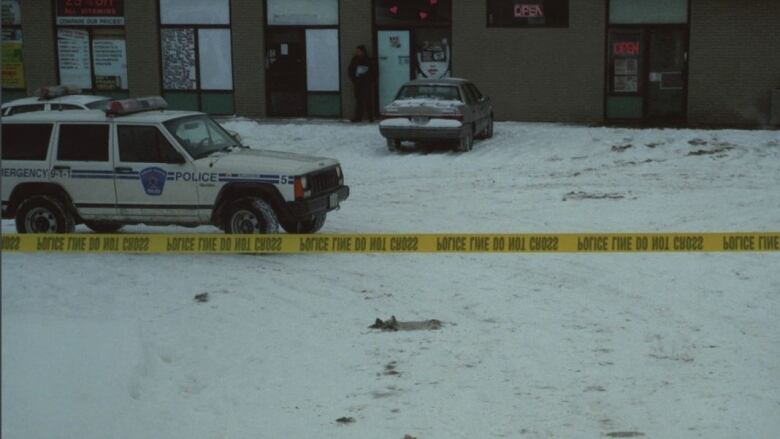 Police photo showing a Sudbury Regional Police truck in a snowy parking lot, marked off with police tape and a beige car parked in front of a strip mall 