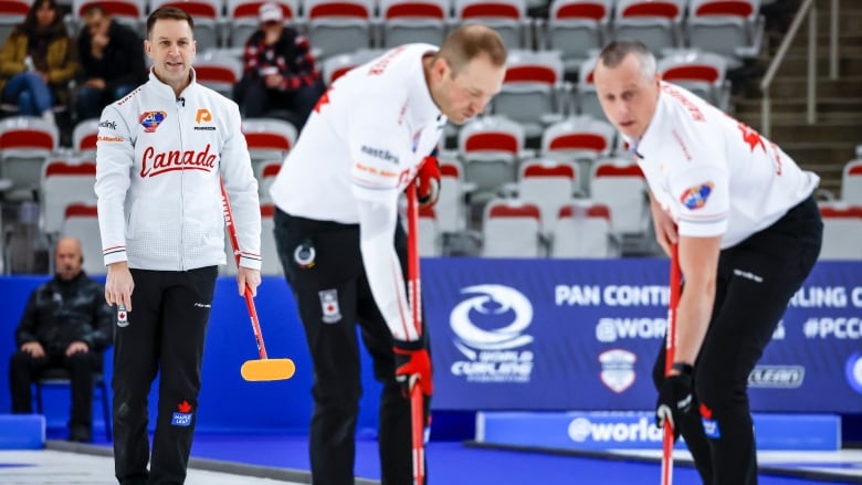 A male curler directs his two teammates that are sweeping the rock.