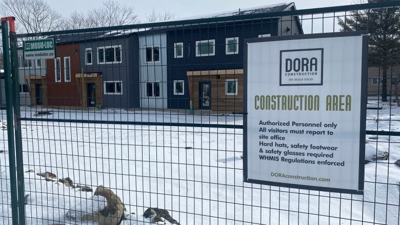 Townhomes are shown behind a wire fence with a sign indicating the project is one being built by Dora construction.