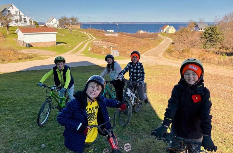 A group of kids on bikes stand outside in front of the ocean.