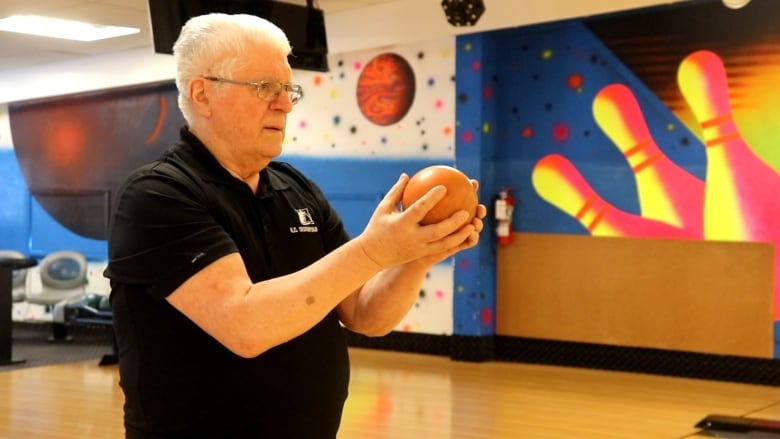 A man holding a orange bowling ball which he prepares to throw down the lane.