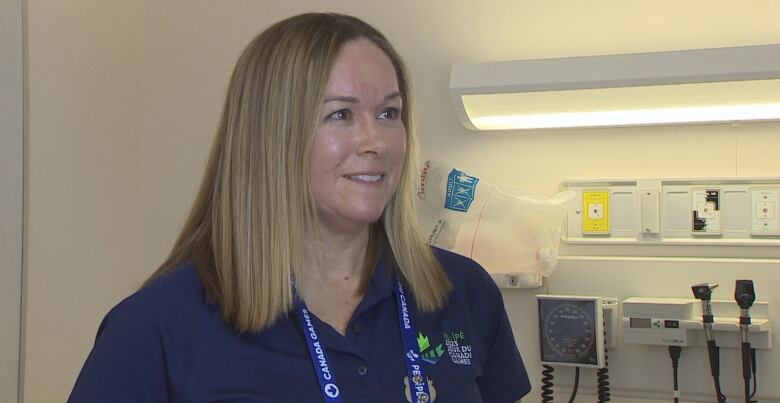 A woman in blue medical scrubs smiles as she stands in a treatment room.