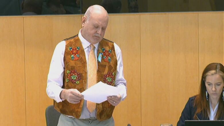 Man in suede vest, standing at desk. 