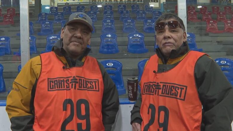 Two men wearing bright orange vests look into the camera.