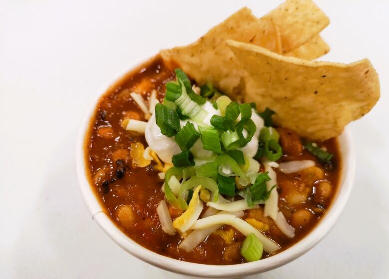 A bowl of chili topped with sour cream, green onions and garnished with tortilla chips