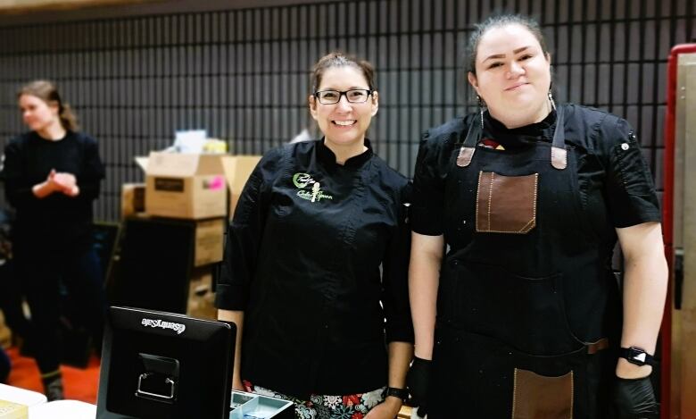 Two Indigenous chefs stand with black aprons