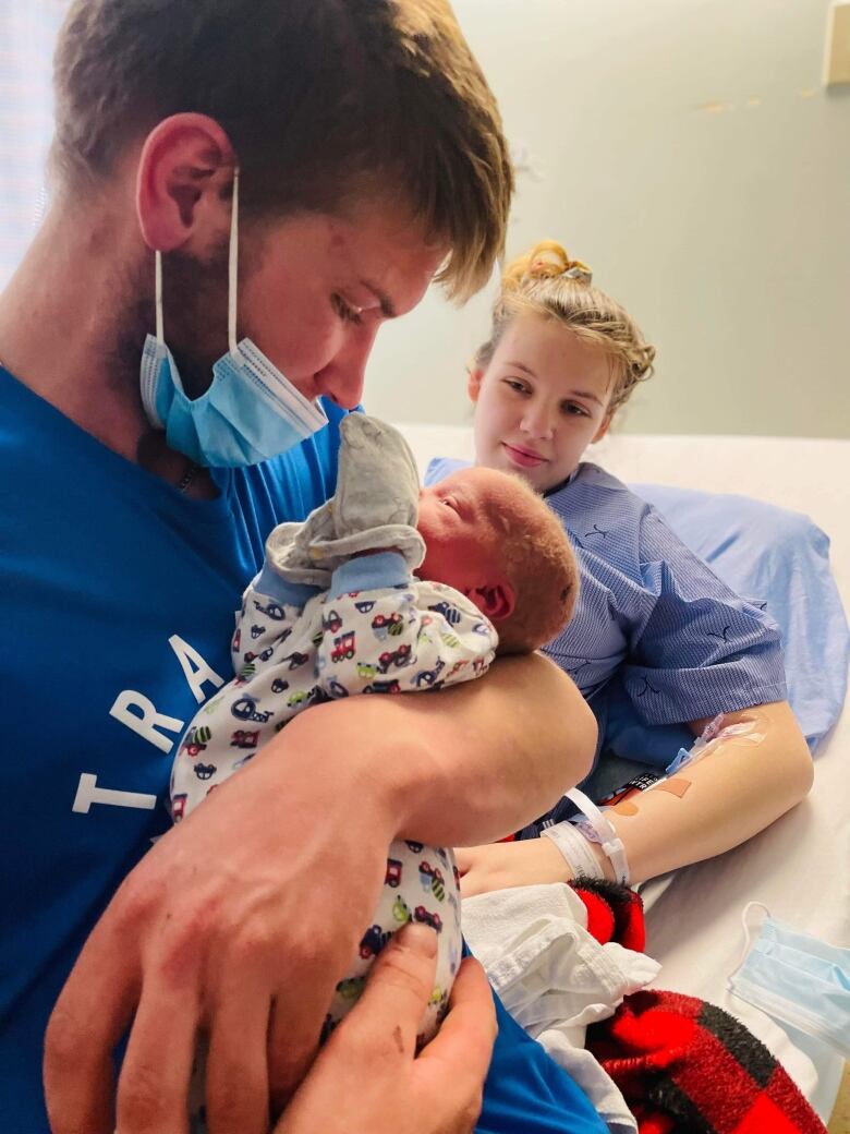 man holding newborn, woman looks on