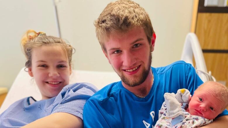 Smiling woman and man on hospital bed, man holding newborn baby