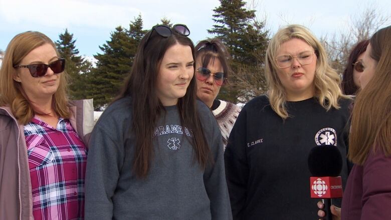 Four women stand outside wearing sweaters.