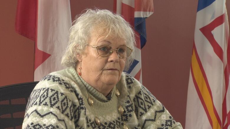 A woman wearing glasses and a knitted sweater sits at a desk.