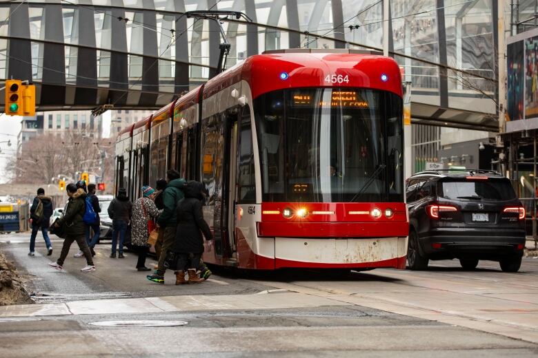 People board a streetcar at a busy downtown intersection.