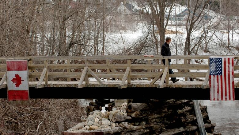 A man walks on a bridge from one side with a Canadian flag to the other side that has a U.S. flag.