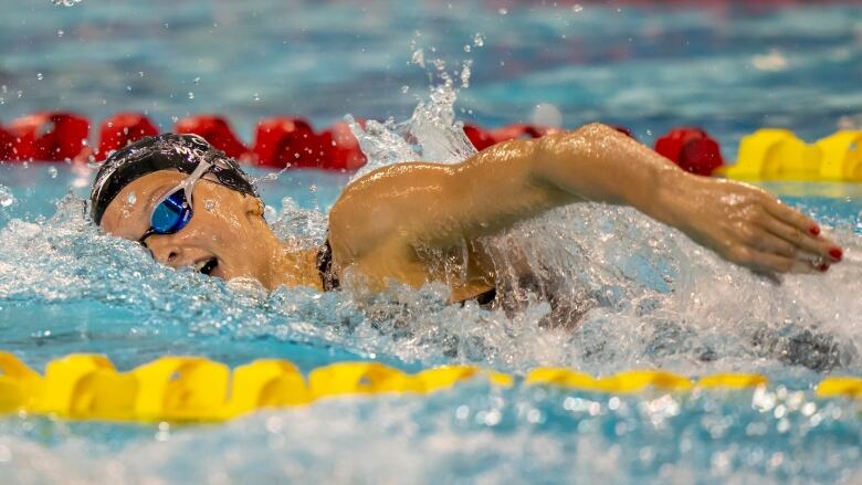 A female swimmer takes a breath with the left side of her mouth while speeding through the water during a freestyle event.