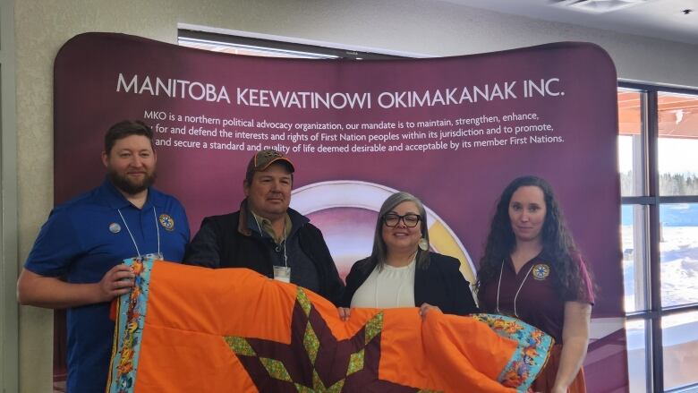 A group of four people hold up an orange star blanket.