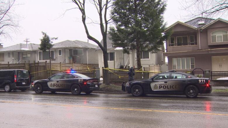 Houses are pictured on a residential street with two police cars stationed out front and police tape. 