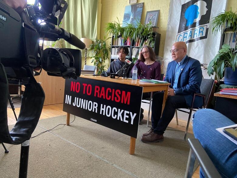 Three people speak behind a table.