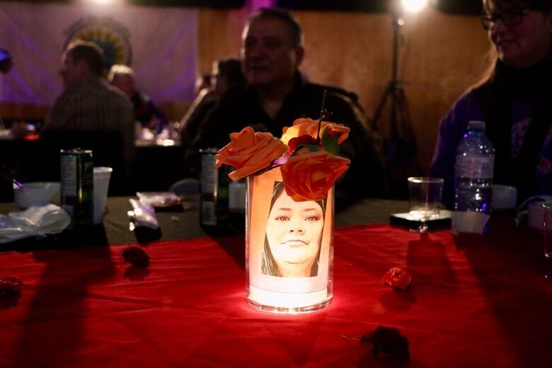 A woman's photo is placed in a vase holding a light and flowers.