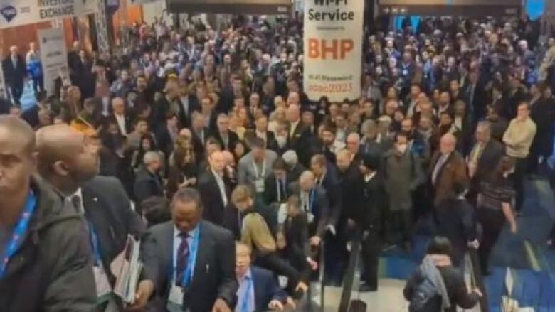 Crowds mingle on an escalator in a crowded convention centre lobby.