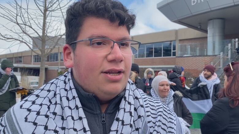 A man wearing a keffiyeh speaks to the camera.