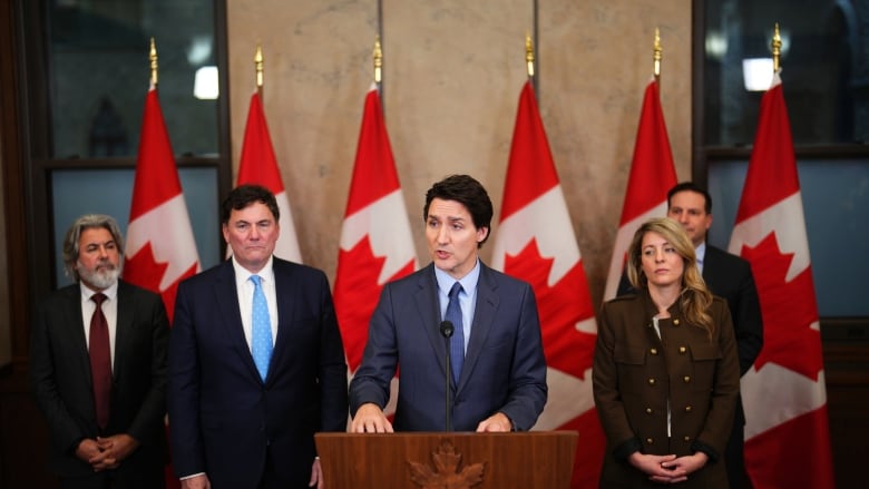 A man speaks while standing at a lectern, flanked by other men and women.