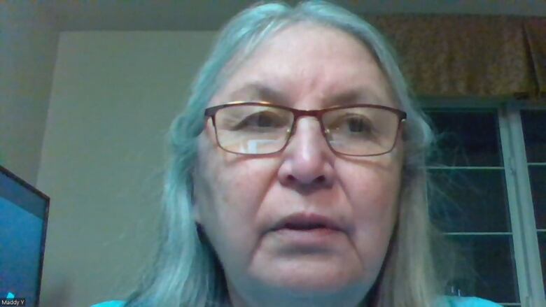 Close up of a woman's face. She has long white hair and wears glasses.