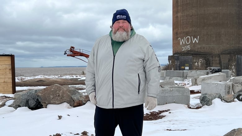 A man wearing winter clothes stands outside on a snowy seashore.