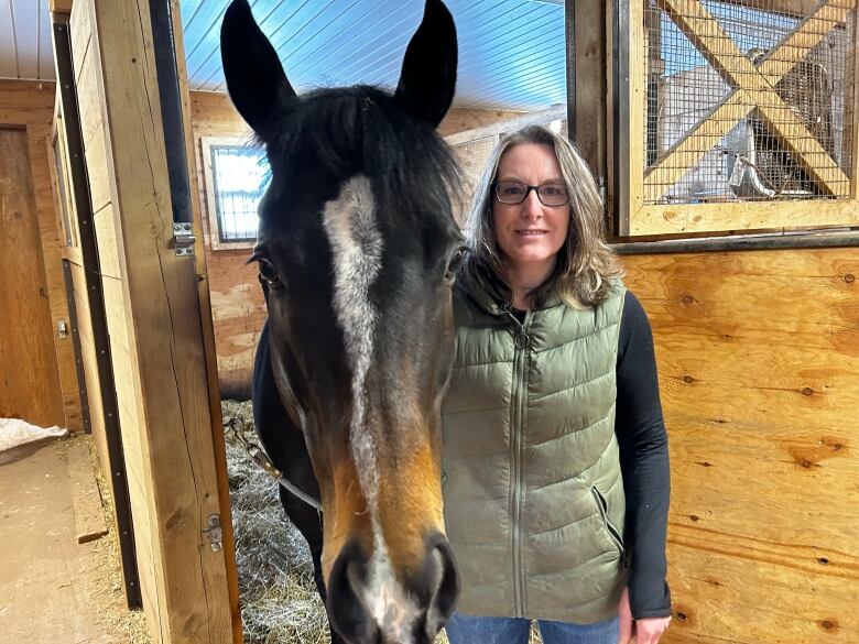 A woman stands with a brown and white striped horse in a stable.