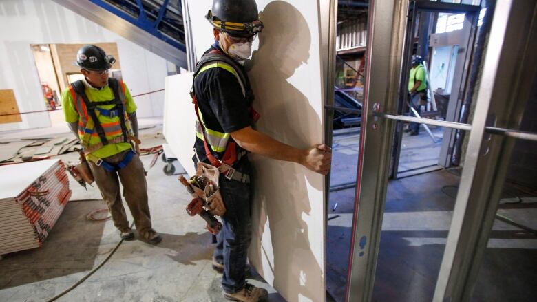 Construction workers install sheets of drywall.