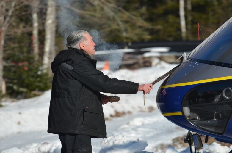 A man holds a feather in front of a helicopter.