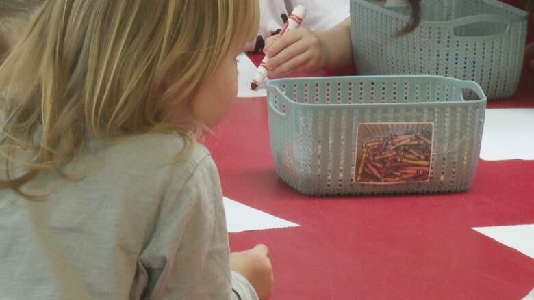 A young child draws with a marker as another looks on.