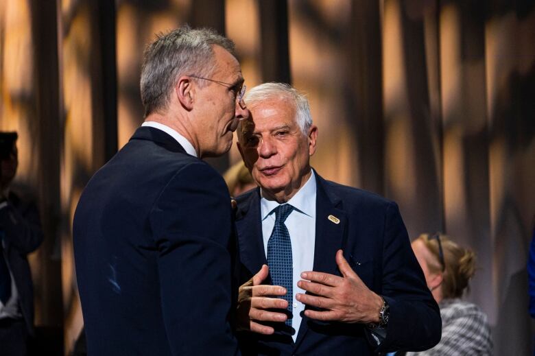 Two men in suits are shown standing in conversation.