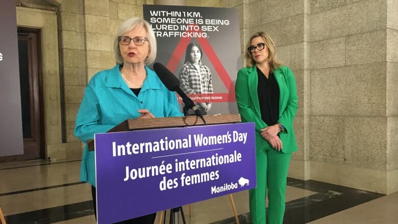 A women speaks at a podium with another woman standing to the right of the podium.