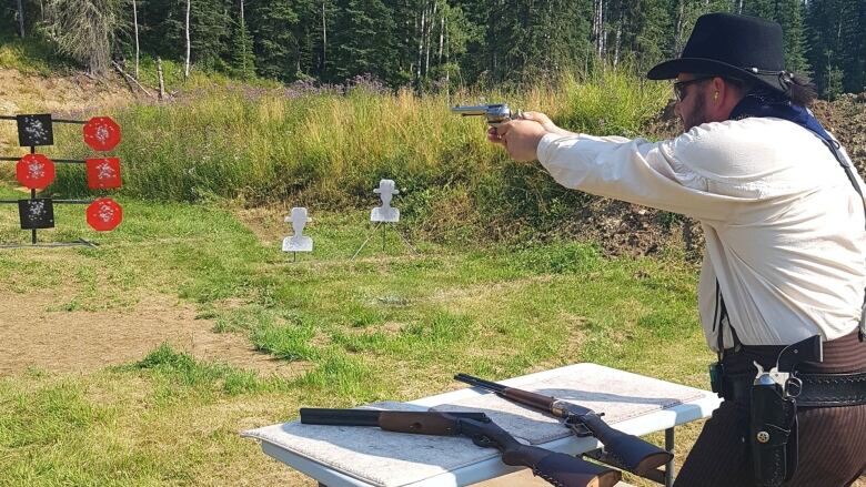 A man dressed as a cowboy fires a gun.