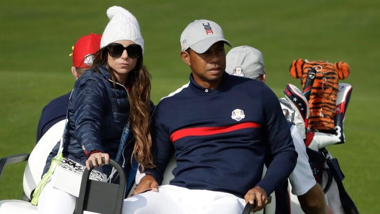 A man and woman in USA gear sit next to each other on the back of a golf cart.