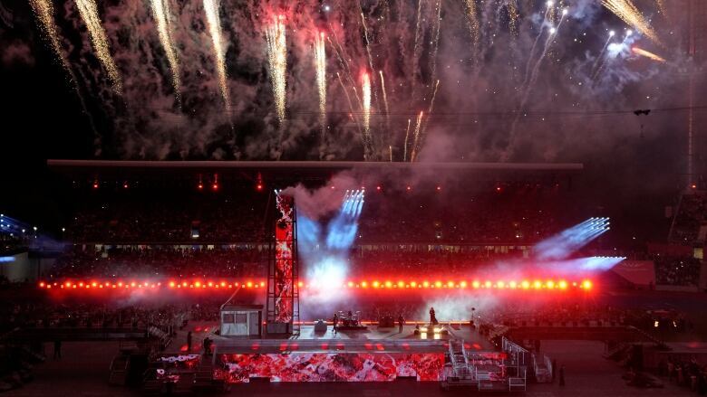 an audience looks out at a red stage there are 13 fireworks exploding in the sky