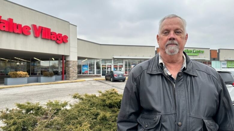 A man stands in front of storefronts.