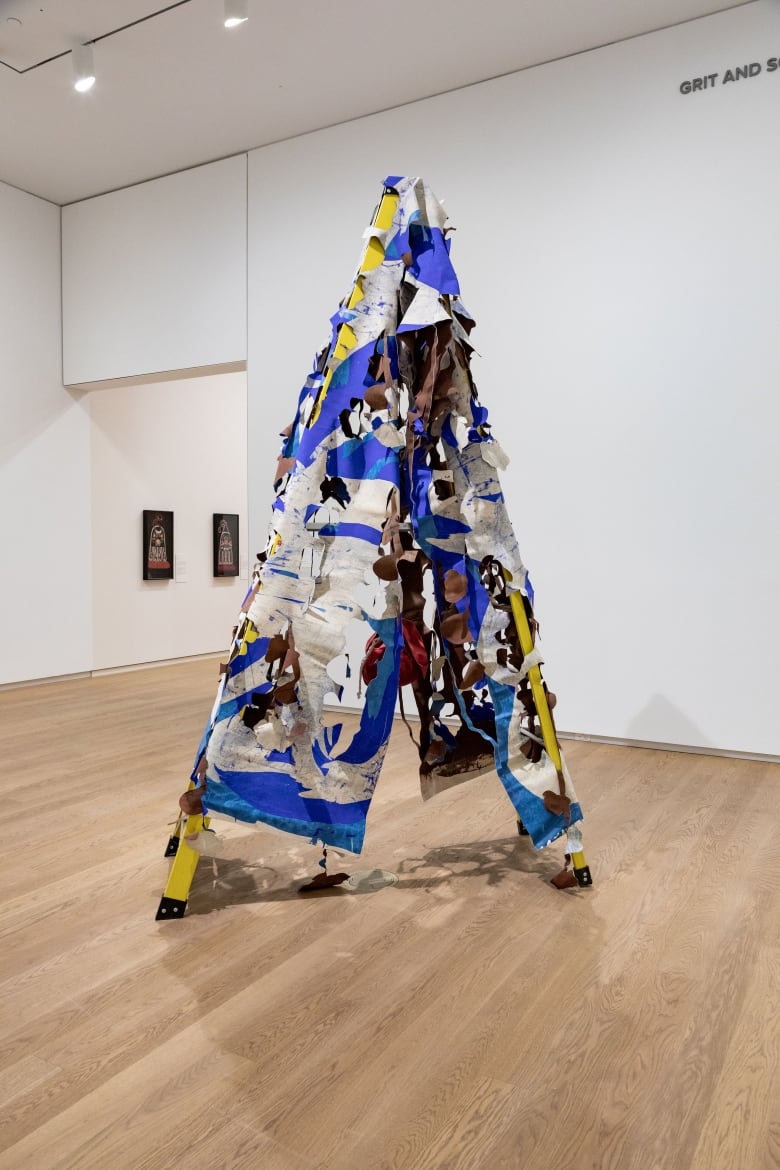 A wooden art structure in the shape of a tall triangle, or a teepee, with a white and blue tapestry over it.