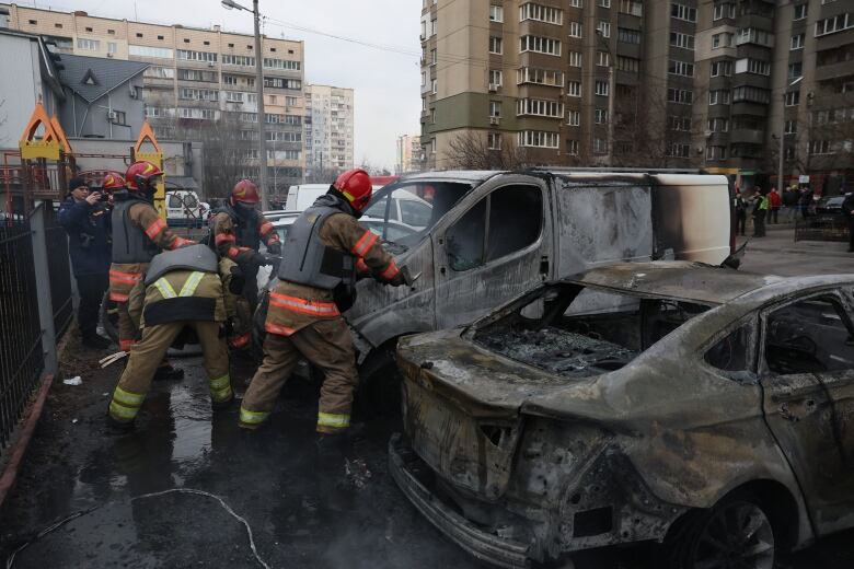 Rescue workers in red helmet and uniforms move around a small car that has been badly burned in a missile attack in Kyiv.