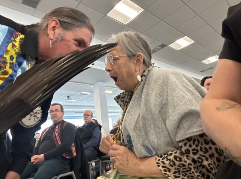 A man holding a feather bends over a woman whose mouth is open in song.