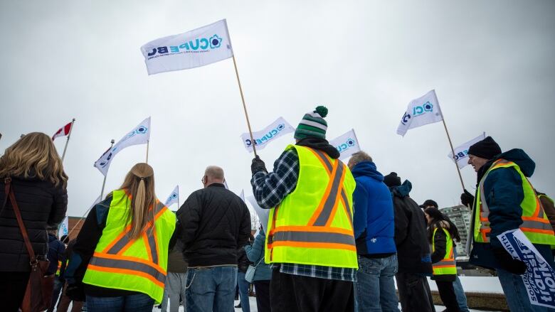 People in yellow vests wave flags with their union's logo.