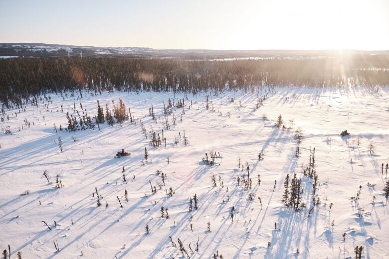 Two people riding snowmobiles across a snowy landscape. 