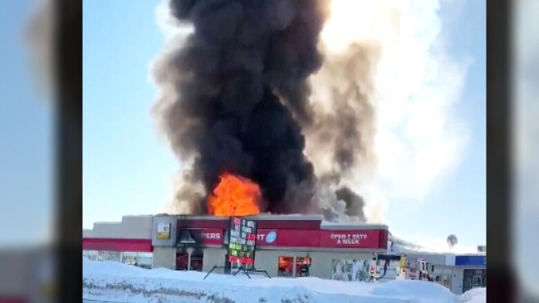 A large orange flame comes out of a Shoppers Drug Mart store in winter as black smoke billows around it.