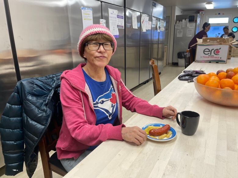 A woman sits at a table with a plate of food and a mug in front of her.